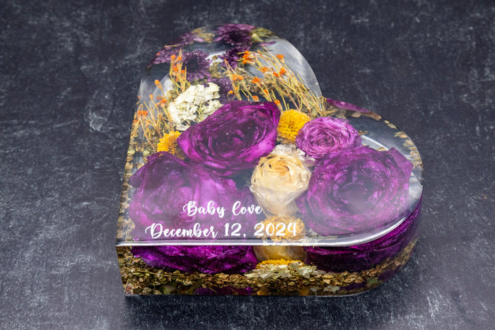 Heart-shaped display case with purple and white flowers on a dark background