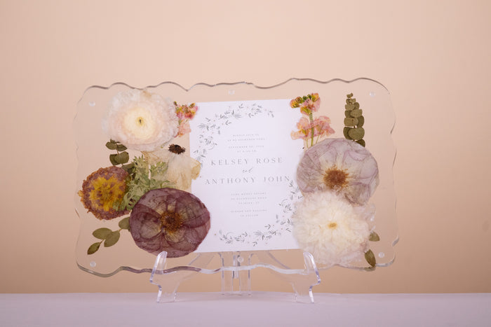 Resin geode tray with pressed wedding flowers and eucalyptus framing a personalized invitation, displaying preserved bouquet blooms in clear epoxy.