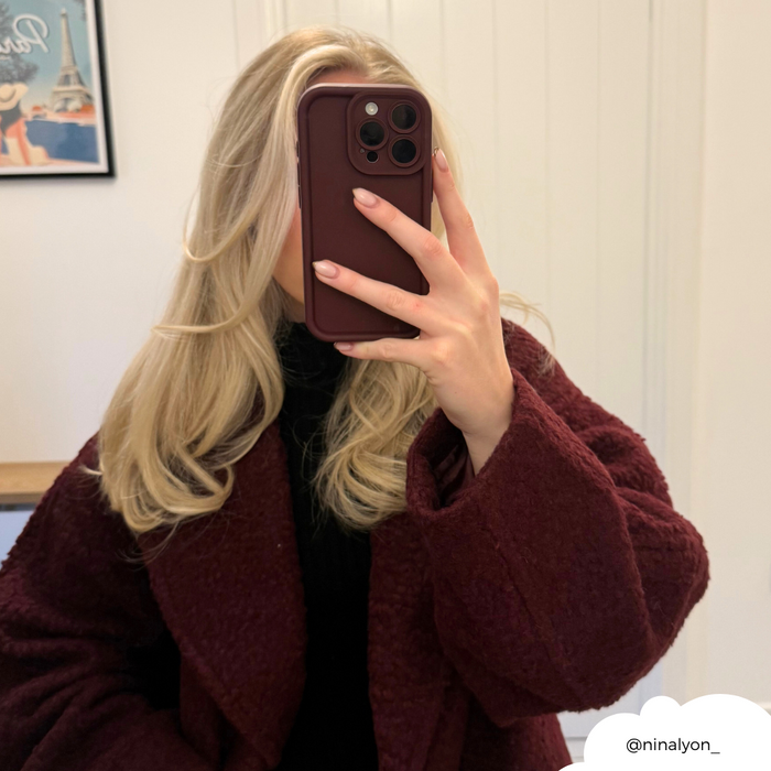 Blonde woman in burgundy coat taking a mirror selfie, phone covered by a burgundy Cloud Soft NAKD case.