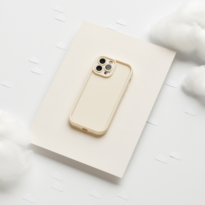 Beige iPhone in a cream Cloud Soft NAKD case on white paper decorated with cloud-shaped cutouts.