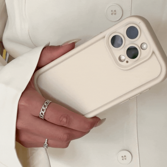 Hand with rings holding a cream Cloud Soft NAKD phone case, matched with a cream blazer.