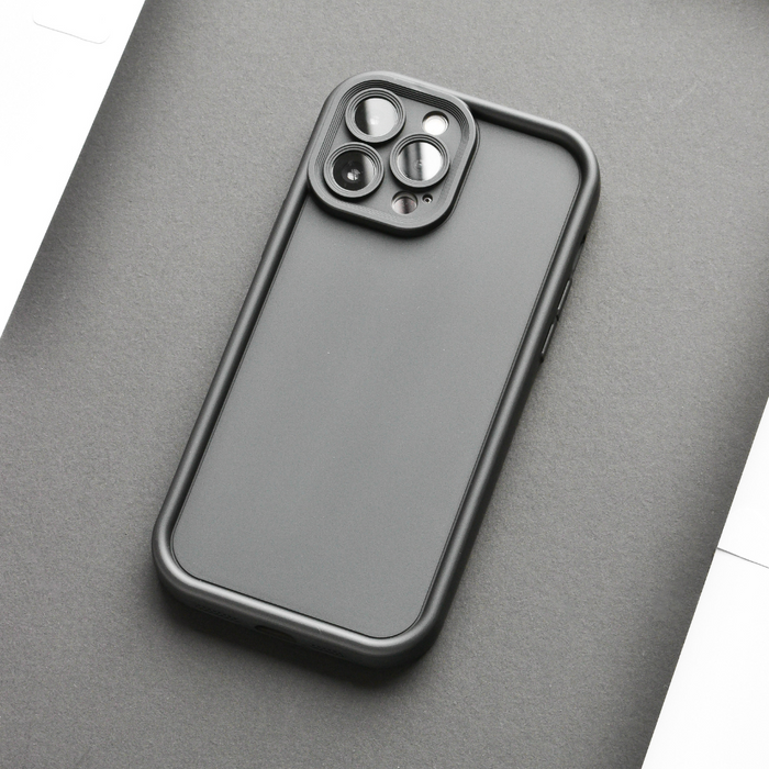 Black iPhone in a Cloud Soft NAKD Kohl Black case on a gray surface, camera visible.