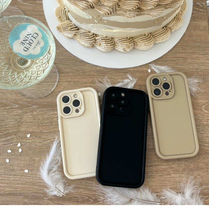 Three iPhones with Coconut Lane Cloud Soft NAKD cases in pebble beige on a wooden table alongside cake and flower petals.