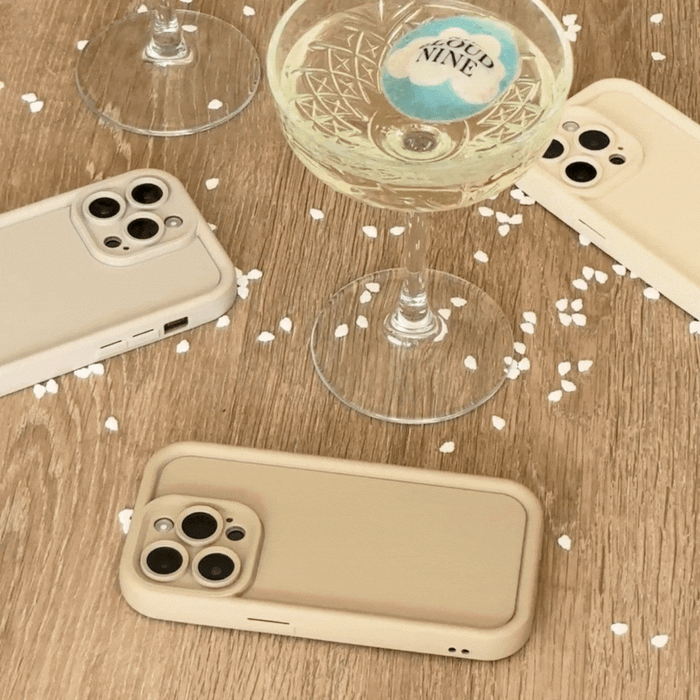 Pebble beige Cloud Soft NAKD phone cases by Coconut Lane on a wooden table with champagne glasses and confetti.