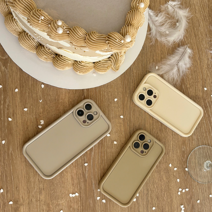Three Pebble Beige Cloud Soft NAKD phone cases on a wooden table beside a beige cake, feathers, and confetti.