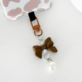 Brown Coquette Bow phone keyring next to a pink and white cow print case.