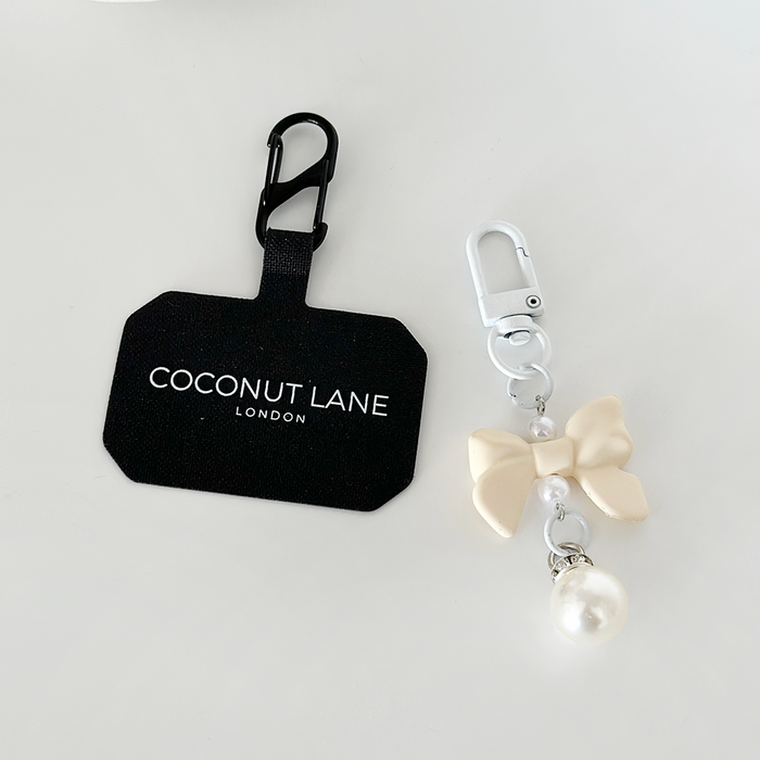 Cream Coquette Bow phone keyring with pearl charm, displayed beside a black Coconut Lane branded tag.