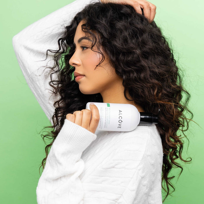 Woman holding a bottle of Curl Leave-In Conditioner with a green background