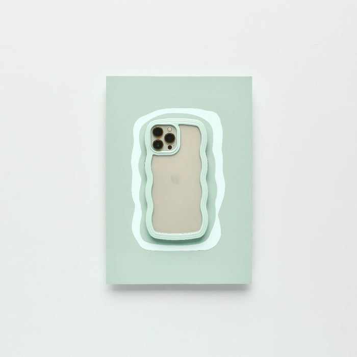 A modern iPhone 15 with a beige back and three camera lenses is placed on a pastel green rectangular surface. The surface features an irregular white and mint green outline, complementing the minimalistic setting. It is protected by the Mint Curvy Phone Case from Coconut Lane.