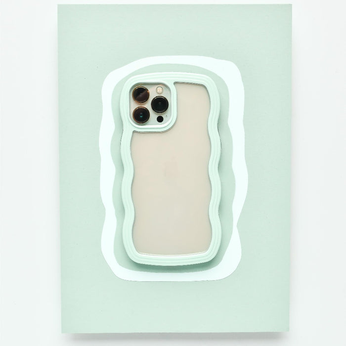 A mint green Curvy Phone Case - Mint by Coconut Lane with wavy edges holds an iPhone 15 featuring three cameras on the back. The protective case is set against a matching light green wavy background, creating a layered visual effect.