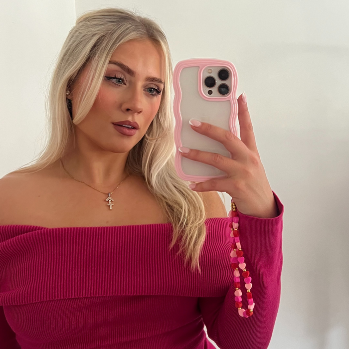 Woman with long blonde hair wears a pink Barbie top and holds a pink curvy Coconut Lane phone case in a mirror selfie.