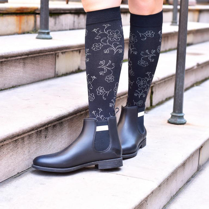 Knee-high compression socks with a floral pattern, worn with black ankle boots on outdoor steps.