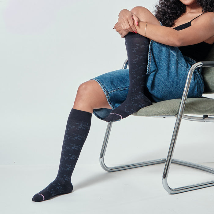 Knee-high compression socks with a floral texture, worn by a person seated on a chair.