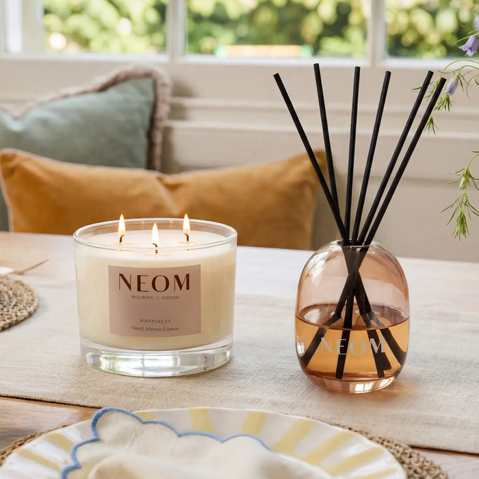 NEOM Happiness scented candle and reed diffuser styled on dining table.