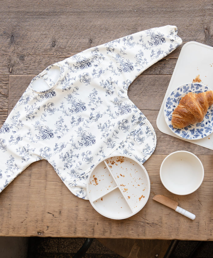 Blue floral toile bib with sleeves and back buttons.