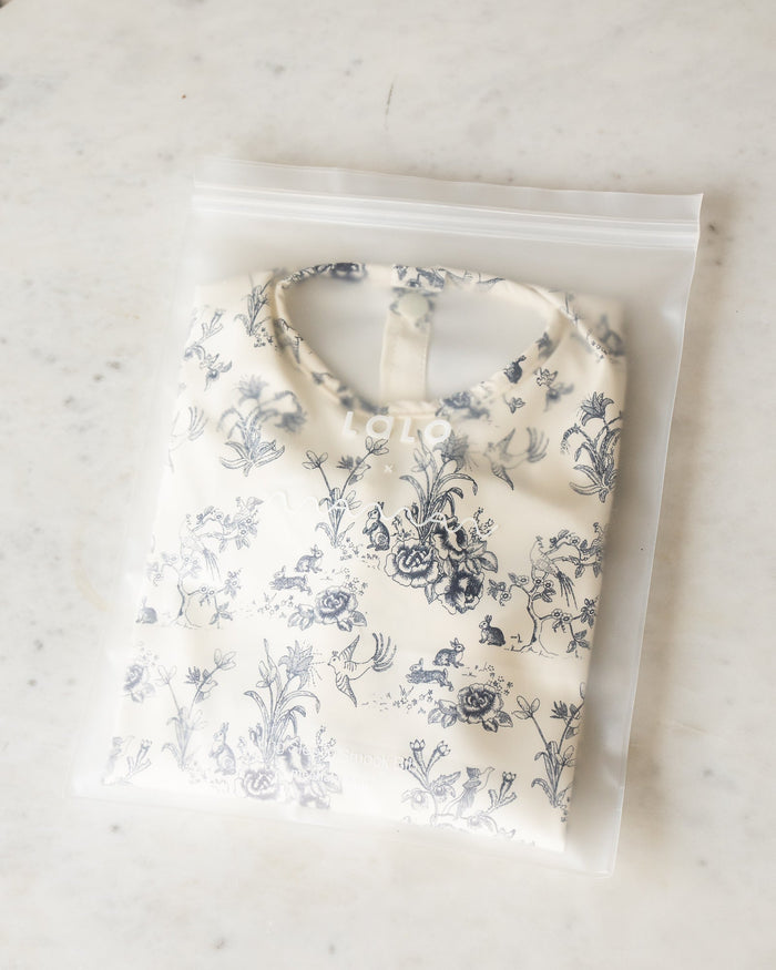 Blue floral toile bib with sleeves and back buttons, folded in a plastic bag with both “LALO” and “Maman” logos.