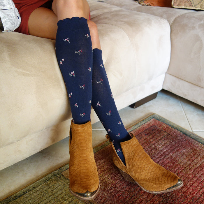 Knee-high navy compression socks with floral patterns, worn with brown ankle boots on a beige couch.