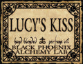 Label for 'Lucy's Kiss' hand blended perfume oil by Black Phoenix Alchemy Lab with decorative border.