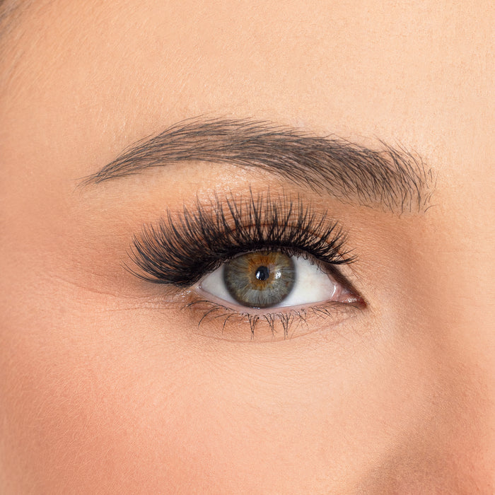 Close up of a green eye with thick false lashes and groomed eyebrow
