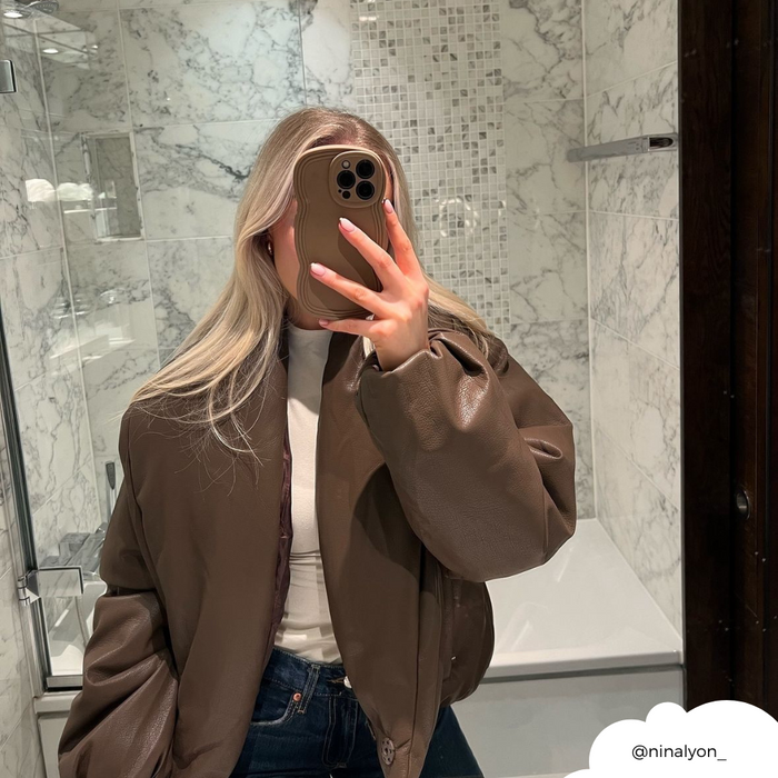 Woman with long blonde hair takes a mirror selfie holding a brown Coconut Lane NAKD Curvy Phone Case.