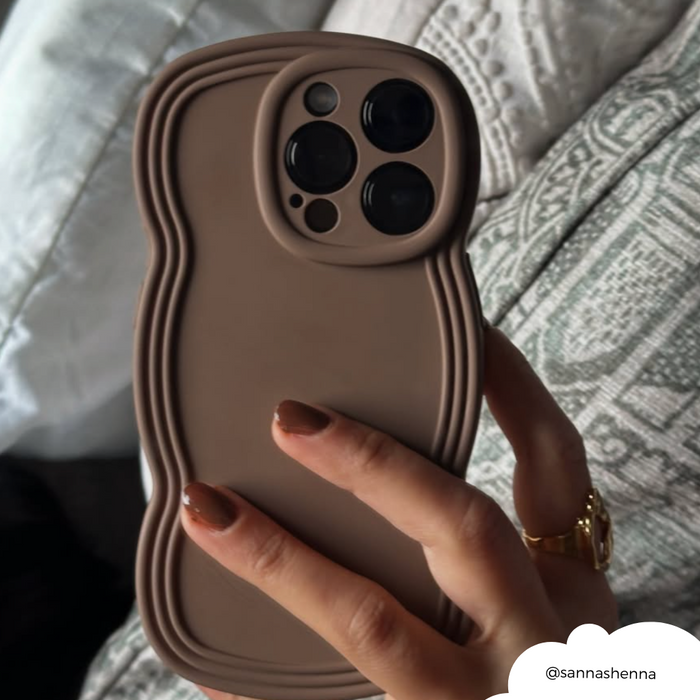 Hand holding phone in Coconut Lane NAKD Curvy Coffee phone case, shown in front of patterned cushions.