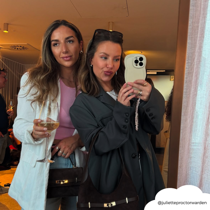 Two women take a mirror selfie; one holds a drink, the other displays a vanilla Coconut Lane NAKD Curvy phone case.