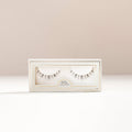 Precious lower lashes displayed in a white box with window on a light beige background.