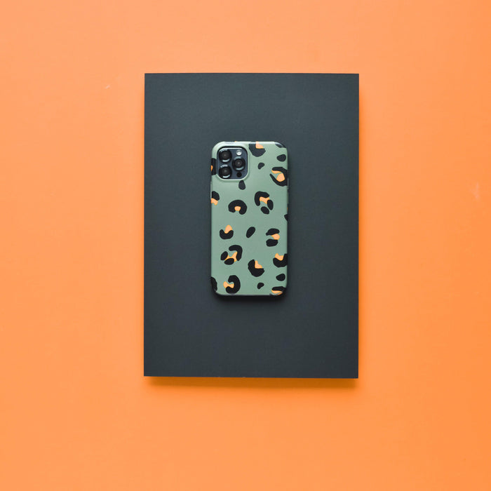 Smartphone in a green leopard print case with a black Coconut Lane lens cover on black, against an orange background.