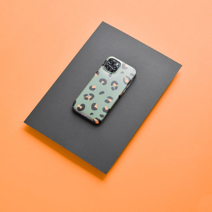 Green leopard print iPhone with black Coconut Lane camera lens covers on an orange background.
