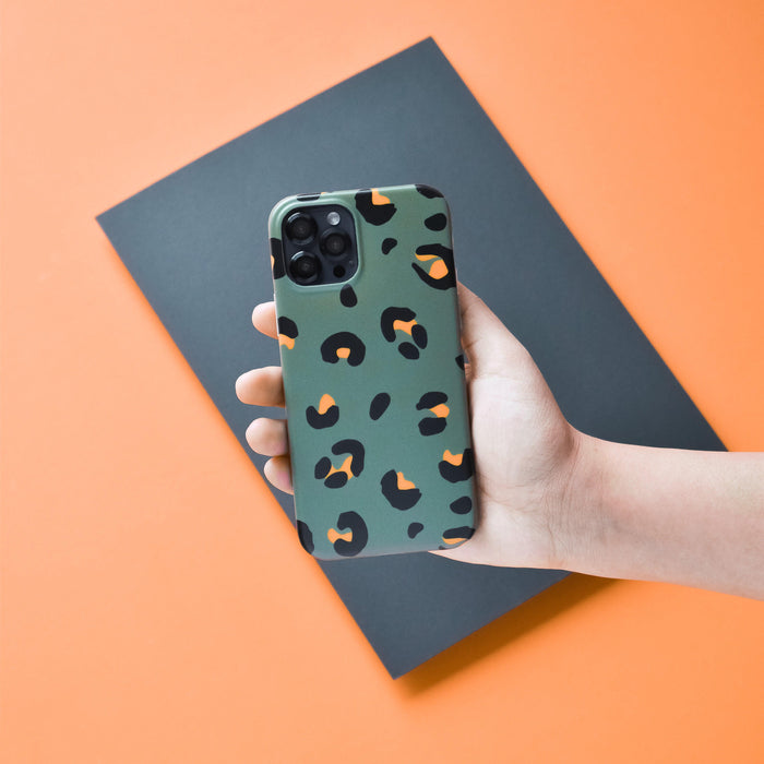 Phone with a green and orange leopard print case and black Coconut Lane camera lens covers held in a hand.