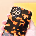 Smartphone with gold glitter Coconut Lane camera lens covers held in a hand, yellow background.