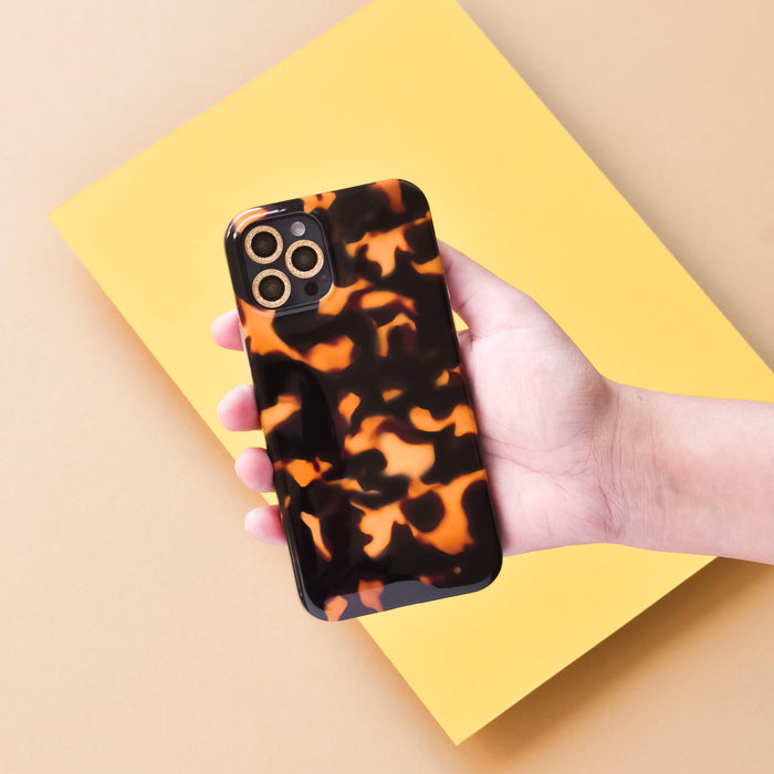 Hand holding a smartphone with gold glitter Coconut Lane camera lens covers, set against a yellow and beige background.