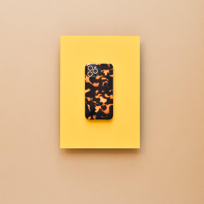 Smartphone in tortoiseshell case with gold glitter lens cover on a yellow surface, beige background.