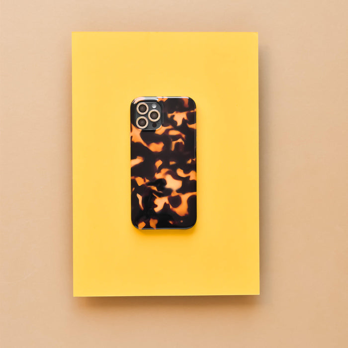 Phone with tortoiseshell case and gold glitter camera lens covers on a yellow sheet.