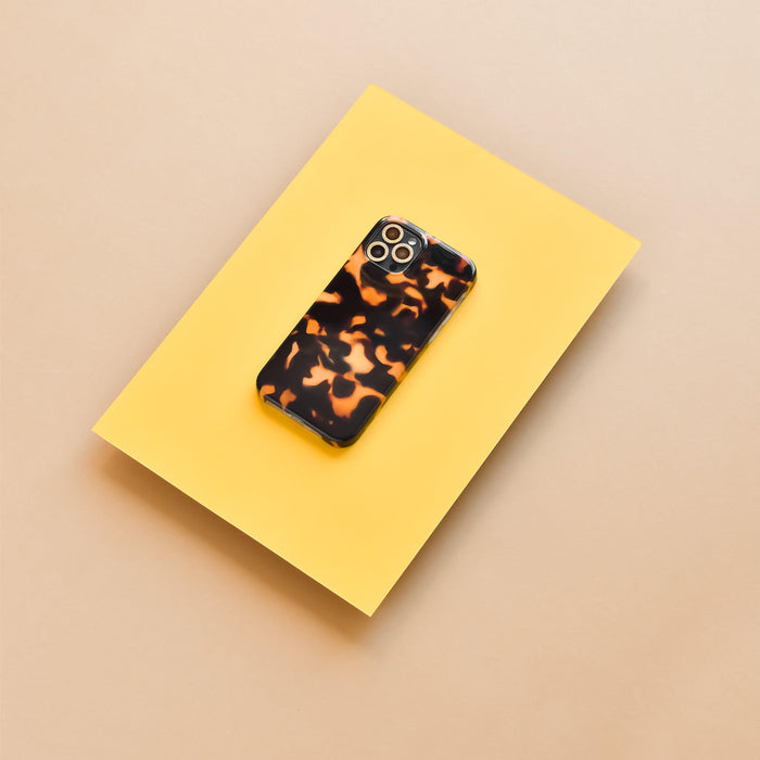 Smartphone with brown tortoiseshell case and gold glitter camera lens covers on a yellow sheet.