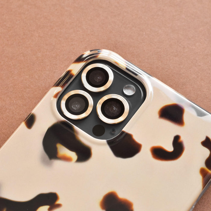 Smartphone with gold Coconut Lane camera lens covers resting on a brown surface.