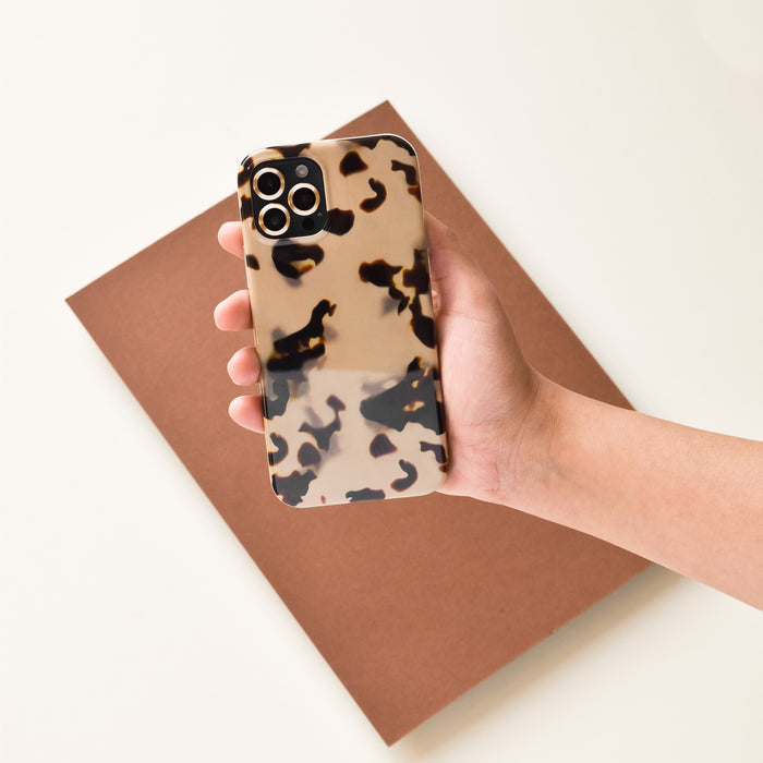 Phone with brown tortoiseshell case and gold camera lens covers held in hand over a folder.