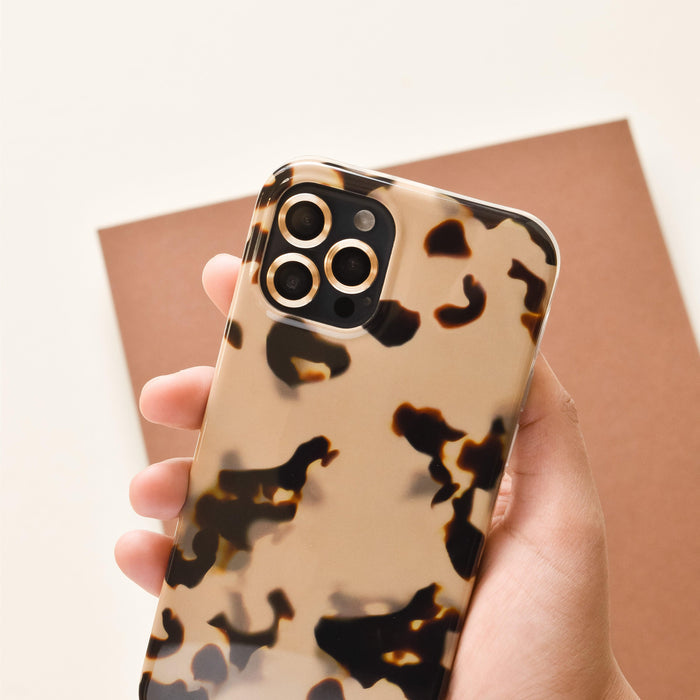Gold Coconut Lane camera lens covers on a smartphone, held in a hand against a brown background.