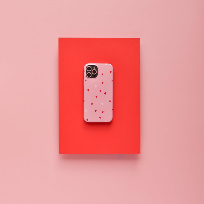 Pink glitter Coconut Lane camera lens cover on a pink phone with red hearts, placed on a red and pink background.
