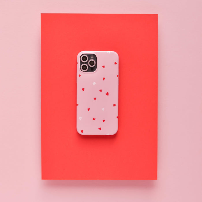 Pink glitter camera lens cover with pink phone case and red hearts on a red rectangle background.