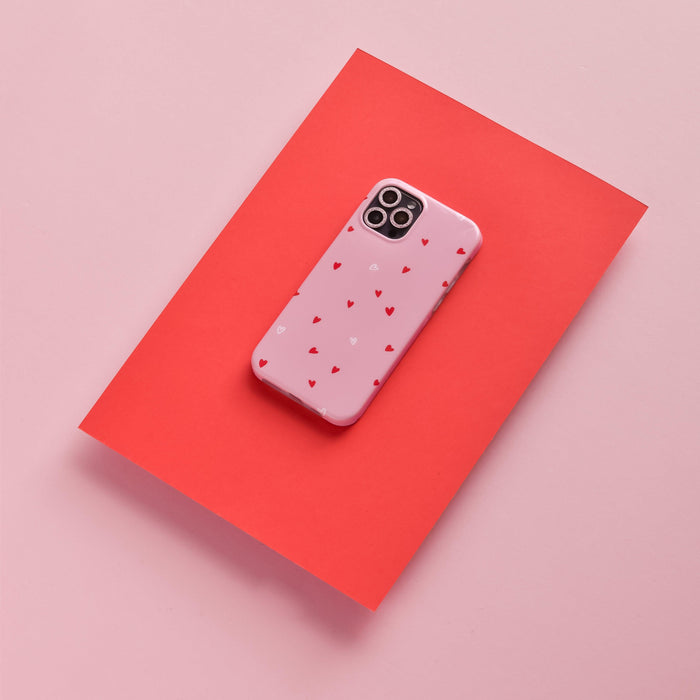 Smartphone with pink glitter camera lens covers and a pink heart case, displayed on red paper.