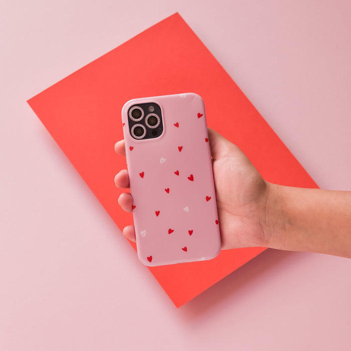 Hand holding pink glitter camera lens covers by Coconut Lane with a red and pink background.