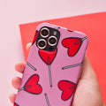Hand holding a phone with a pink case, red heart-shaped lollipops, and pink Coconut Lane camera lens covers.