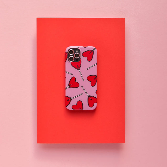 Pink Coconut Lane camera lens cover on a pink phone case with a red heart pattern.