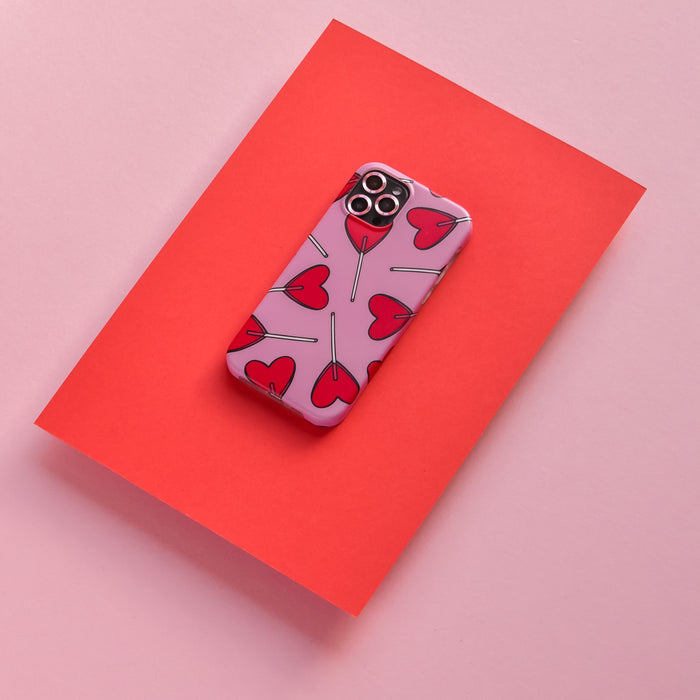 Pink iPhone with Coconut Lane pink case featuring red hearts, on a red sheet with a pink background.