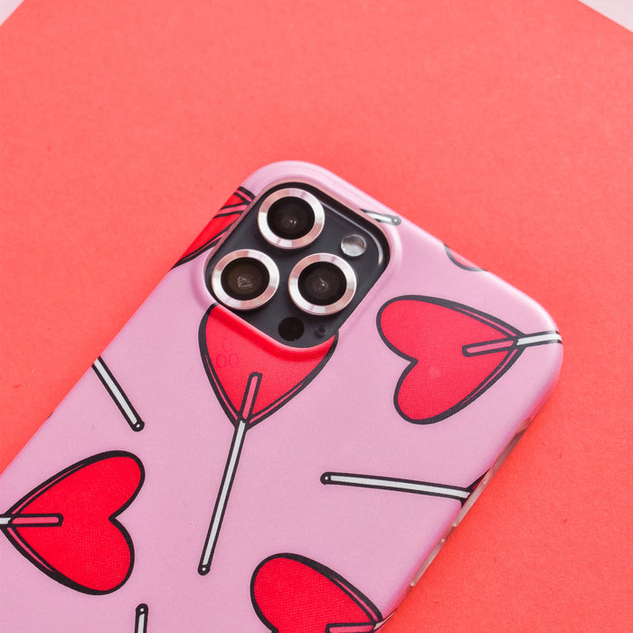 Pink Coconut Lane camera lens covers next to red heart-shaped lollipops on a red background.