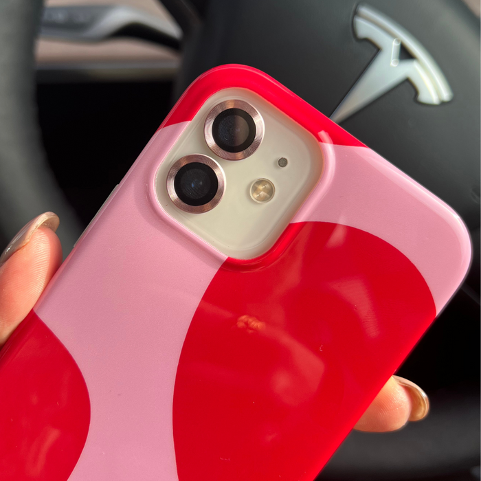 Pink Coconut Lane camera lens cover on iPhone held by hand near a Tesla steering wheel.