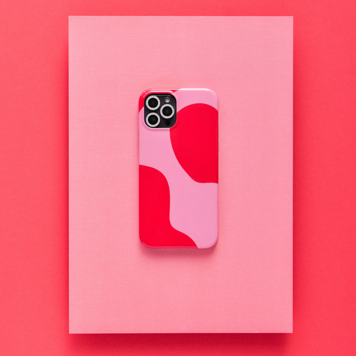 Smartphone with a red and pink abstract case and silver glitter camera lens covers on a vibrant background.