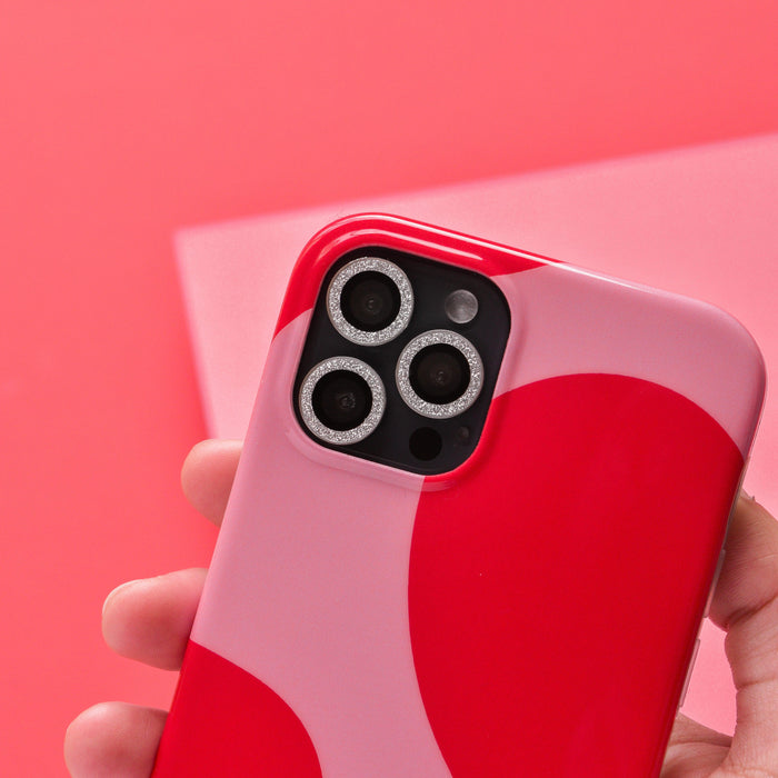 Hand holding a smartphone with silver glitter Coconut Lane camera lens covers against a soft pink background.