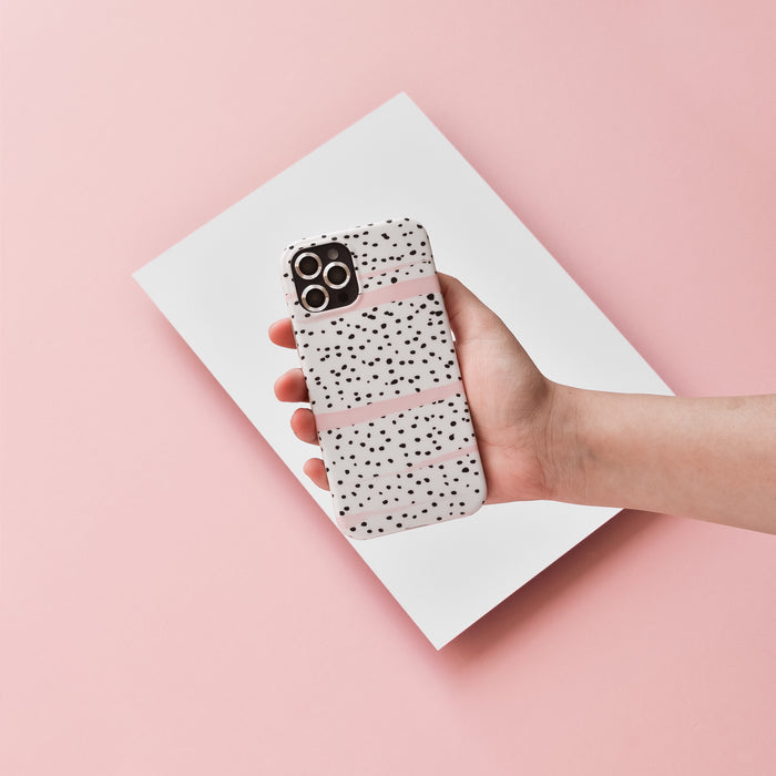 Hand holding a smartphone with silver camera lens covers and a speckled case, set against pink paper.
